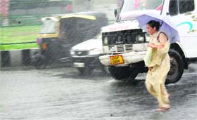 A woman faces hard time crossing a road as it rains heavily in Jammu
