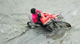 A cyclist crosses a waterlogged road after heavy rain in Patiala on Tuesday.