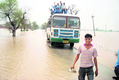 A bus passes through a flooded road in Ayalki village near Fatehabad on Thursday.