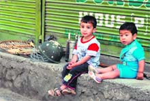 Two children sit in front of a closed shop in Srinagar where a strike was observed on Sunday in response to a call given by separatists.