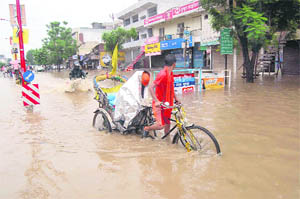 A rickshaw-puller paddles through a water-logged road in Haridwar on Saturday.