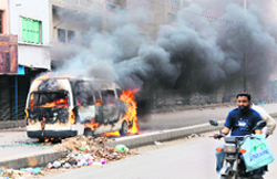 A Pakistani motorcyclist rides past a burning van following overnight violence in Karachi 