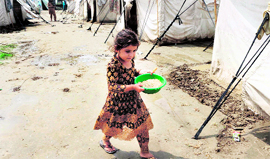 A Pakistani girl displaced by floods carries a bowl of grains through a relief camp in Nowshera on Saturday.