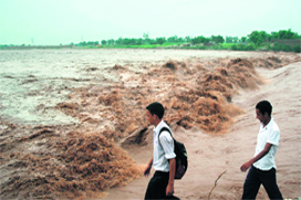 Schoolchildren walk past the raging Tawi in Jamm