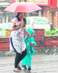 A woman and her child cross a road as it rains in Dehradun