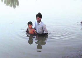 A resident of Jalloke along with his son wades through flood water to reach a safer place