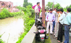 Passers-by look at the scooty that the girl, who fell into the canal, was riding in Kankhal, Haridwar,
