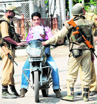 Security men check a motor cyclists curfew pass in Srinagar on Wednesday