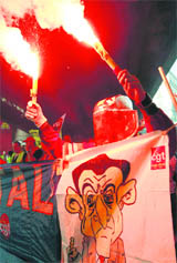 An Arcelor Mittal worker dressed in a protective work suit holds flares and a banner with a caricature of French President Nicolas Sarkozy as he demonstrates over pension reforms in Marseille on Thursday.