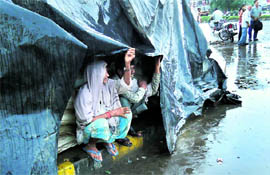 Rickshaw-pullers take shelter under a polythene sheet to protect themselves from rain near Tau Devi Lal Chowk in Karnal