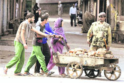 Members of a family carry bricks in a cart as a jawan stops them for checking at a deserted street in Srinagar on Thursday. 