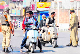 Security personnel stop scooterists to check their curfew passes in Srinagar on Saturday