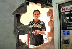 The owner of a cyber cafe shows the broken wall from where thieves entered the cafe and fled with computers in Ludhiana