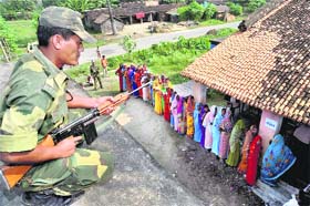 ON GUARD: A security officer keeps vigil as voters stand in a queue to cast their ballots in Samastipur