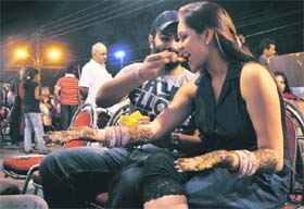 A city resident helps his wife take a bite of steamed corn as she waits for her henna-decorated palms to dry up in Ludhiana