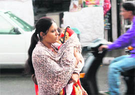 A woman covers her child with a shawl after rain in Jammu