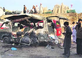 Residents gather near a minibus, which was damaged by a suicide bomb attack, in Kohat