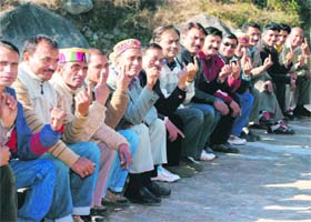 Men sit in a queue after casting their votes in Dari panchayat elections near Dharamsala