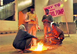 Labourers huddle around a fire to get some respite from shuddering cold alongside a road