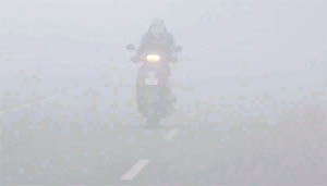A woman wades through heavy fog on her scooter.
