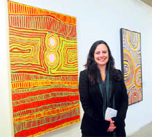Kathryn Deyell standing among (L) Nyaru (by Lucy Loomoo) and (R) Tjukukalyu (by Jimmy Tchooga). Nyaru has two old men Dreaming while Tjukukalyu is set in traditional country by the same name. The central circle represents water and surrounding patterns the sandhills