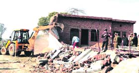 A JCB pulls down an illegal construction under a drive of the Department of Town Planning in Jhajjar