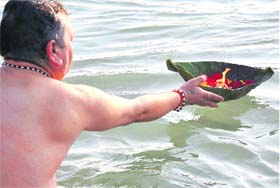 A devotee makes a deepdaan to the Ganga while another reads the Gita