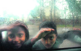 Children peep into a car as rainwater falls on its windowpanes in Jammu.