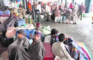 Srinagar-bound passengers sit in the open at General Bus Stand in Jammu after traffic on the Srinagar-Jammu Highway was suspended following incessant rain which triggered a landslide near Panthal. 