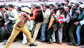 A policeman attempts to control cricket fans jostling to maintain their position after a minor stampede in a queue for tickets ahead of the Cricket World Cup match between India 