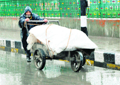 An elderly man carries goods in a cart during rain in Srinagar 