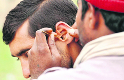 A man gets his ear cleaned from a roadside quack in Jammu