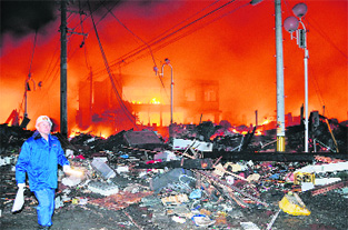 Houses lie flattened after a powerful earthquake in Iwaki, Fukushima Prefecture. A raging fire is seen in the backdrop.