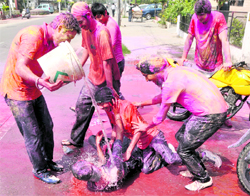 A youth, floored on the road, being poured with water and colours by his friends.