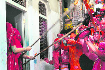 In Lathmar Holi, veiled women chase away the men by hitting them with batons, while the men protect themselves with makeshift shields