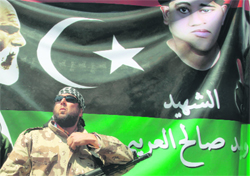 A rebel stands guard in front of a picture of a youth killed in recent clashes, during prayers in Benghazi on Friday