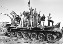 People celebrate atop a destroyed tank belonging to forces loyal to Muammar Gaddafi after an air strike by coalition forces in Ajdabiyah