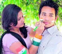 A girl applies paint on the face of a boy in preparation to cheer for Team India