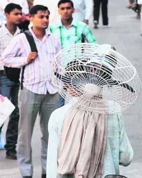 GEARING UP FOR HARSH SUMMER: A man carries a pedestal fan in a busy market in Panipat