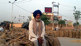 A farmer sits in front of the display board which has been installed at the top of the building of the Punjab Mandi Board Office at Dhanaula in Barnala district.