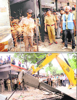 An employee of the MCs enforcement staff removes encroachment with the help of a gas-welding cutter and a JCB machine demolishes illegal shops in the Sector 19 Sadar Bazaar, Chandigarh, on Tuesday. 