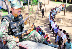 A jawan keeps vigil from a rooftop as voters stand in queues to cast their votes at Barikula in Bankura district of West Bengal on Tuesday