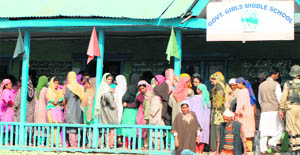 Voters wait for their turn to cast vote at a school at the Trehgam block in Kupwara district