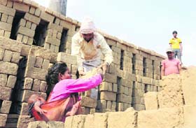 WOMEN EMPOWERMENT ONLY ON PAPER: A woman carrying her child on her back works in a brick-kiln near Jani village in Karnal district