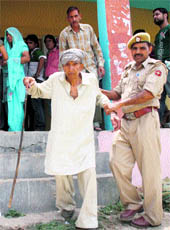A policeman helps Dhuni Chand, who braved hot weather and came out to vote at Aghore in Jammu division on Wednesday