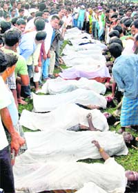 People stand near the bodies of passengers of the bus that fell down into a rivulet near Charabari village in Kamrup district of Assam on Tuesday
