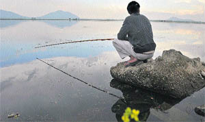 A man sits on a stone as he fishes in Dal Lake in Srinagar 