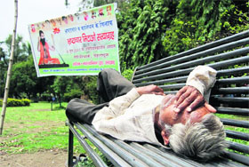 A man enjoys his siesta on a bench near a banner of yoga guru Ramdev hung in Gandhi Park, Dehradun,on Thursday.