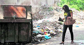 A woman with her face covered walks past a heap of garbage in the Clock Tower ward of Dehradun.