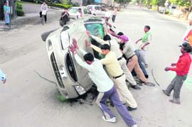 People and a policeman helping a driver to steady a car which had turned turtle at Survey Chowk in Dehradun